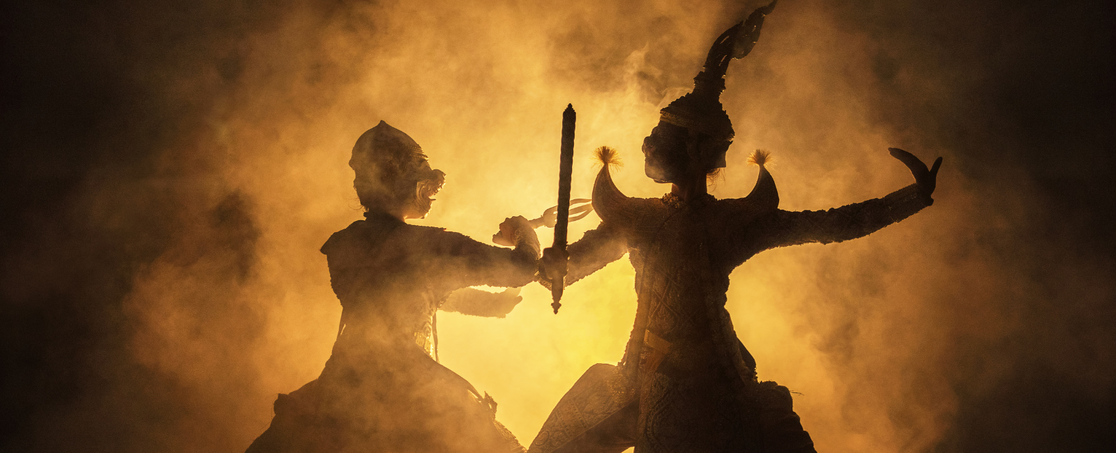 Two costumed players backlit by an orange light during a performance